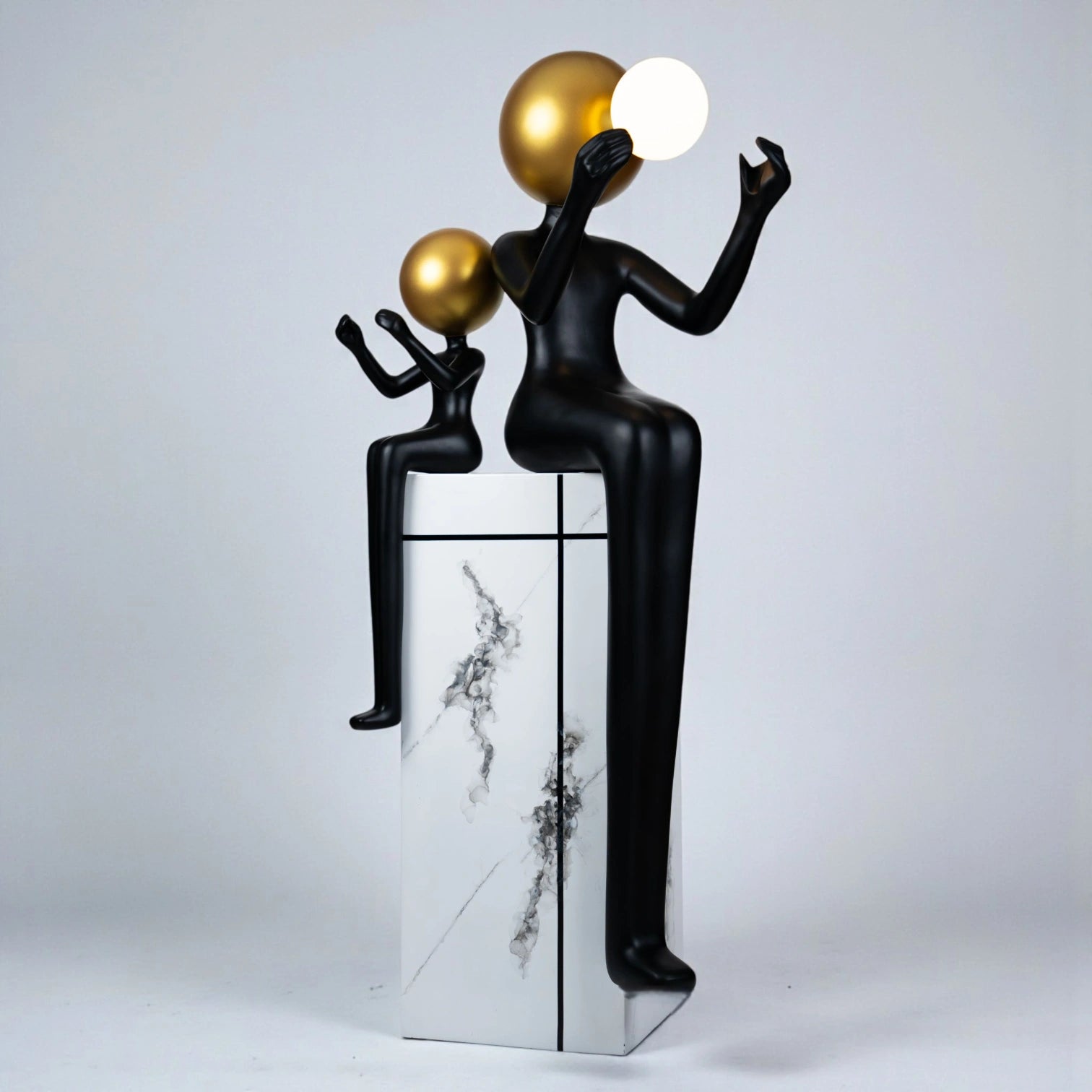 Black and gold human figurine duo holding a glowing orb on a marble pedestal sculpture