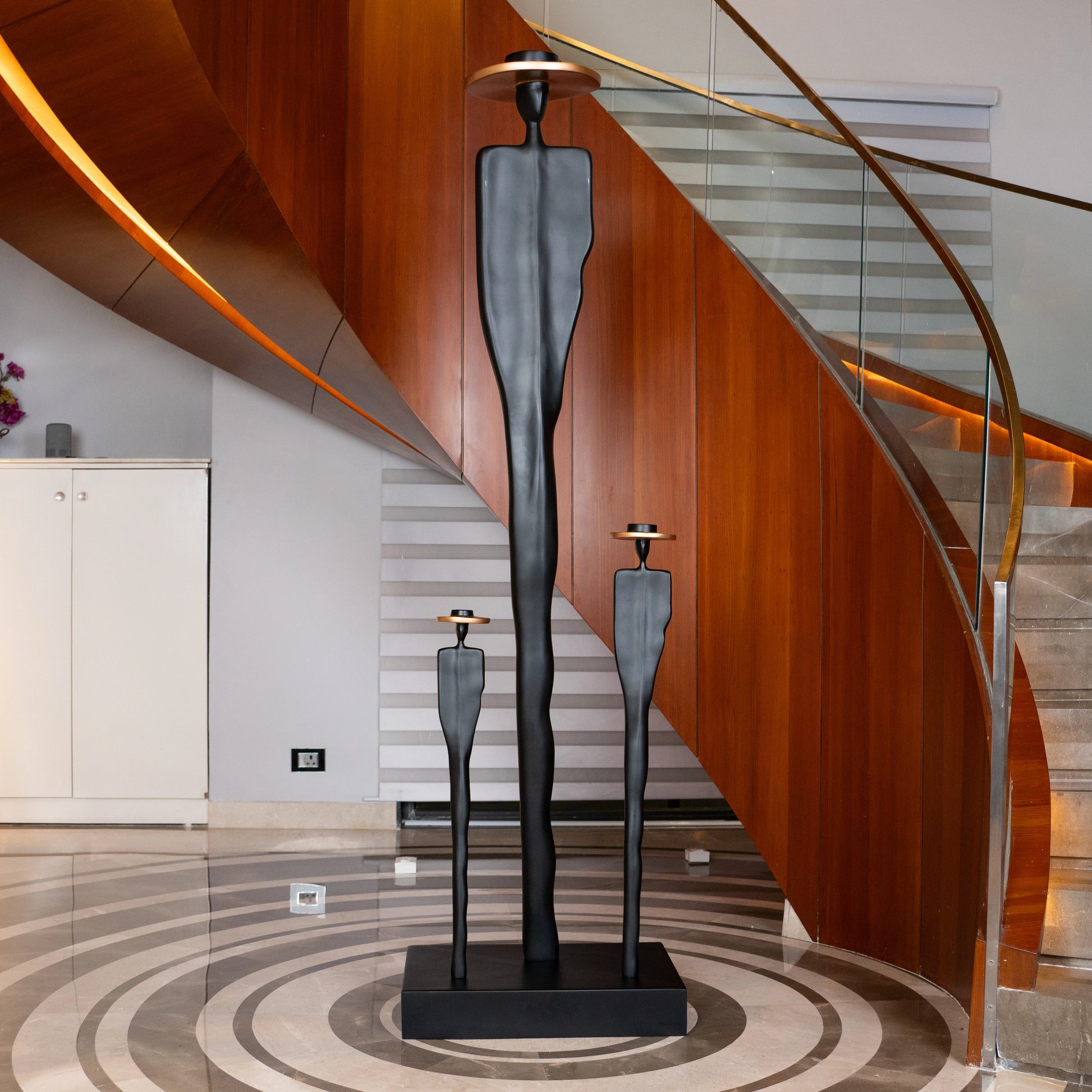 Tall matte black resin sculpture of three elongated human figures with bronze hats — Ethereal Harmony Sculpture by Ghar Art, handcrafted luxury decor symbolizing unity and balance.