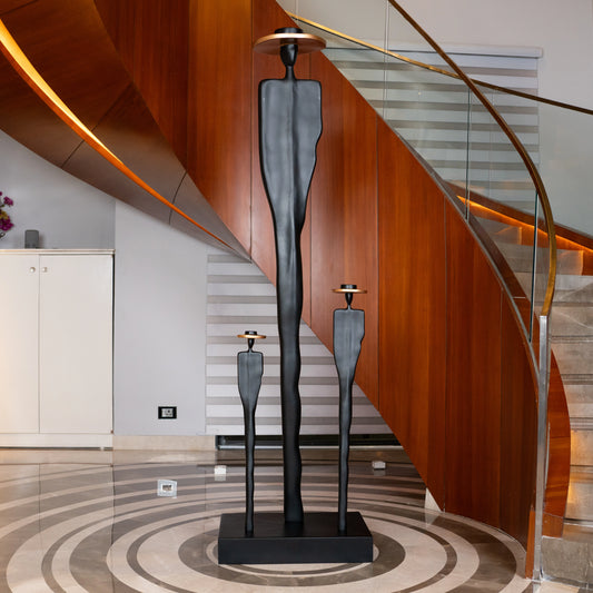 Tall matte black resin sculpture of three elongated human figures with bronze hats — Ethereal Harmony Sculpture by Ghar Art, handcrafted luxury decor symbolizing unity and balance.