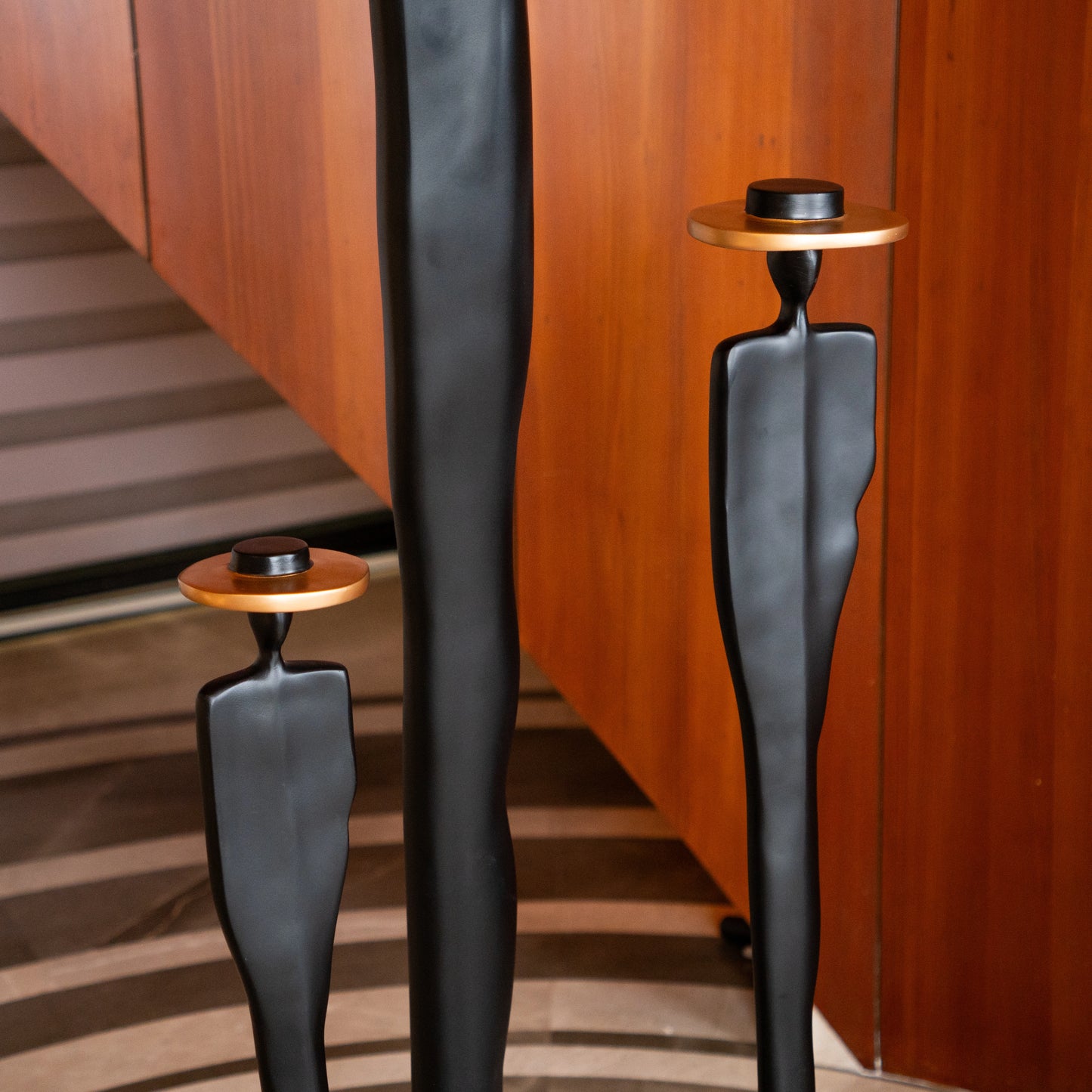 Tall matte black resin sculpture of three elongated human figures with bronze hats — Ethereal Harmony Sculpture by Ghar Art, handcrafted luxury decor symbolizing unity and balance.