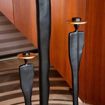 Tall matte black resin sculpture of three elongated human figures with bronze hats — Ethereal Harmony Sculpture by Ghar Art, handcrafted luxury decor symbolizing unity and balance.
