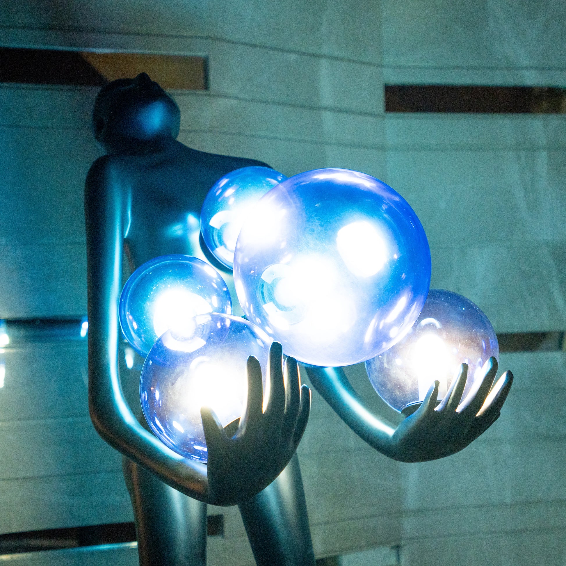 Tall matte black sculpture of human figure holding glowing blue light spheres — Azure Radiance Sculpture by Ghar Art, handcrafted illuminated modern home decor accent.