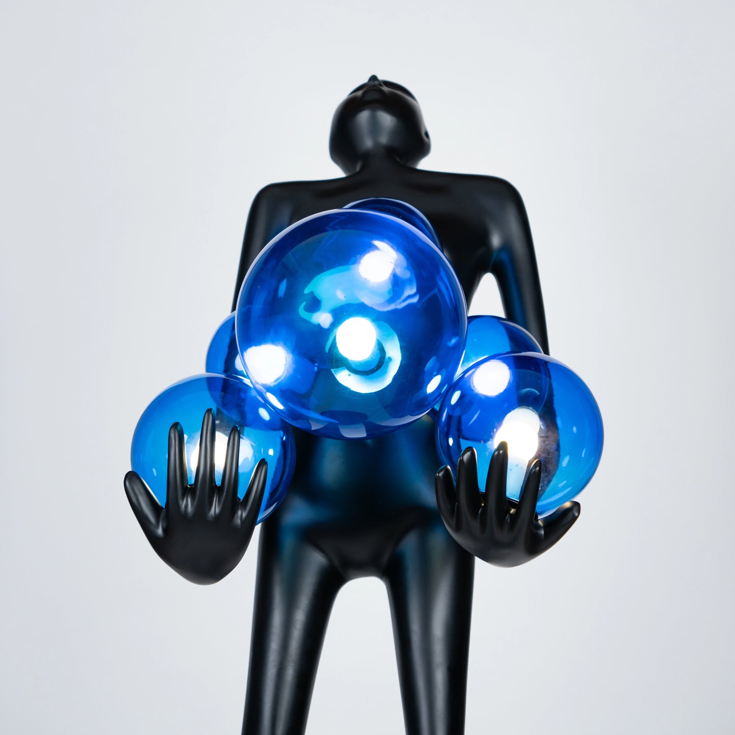 Tall matte black sculpture of human figure holding glowing blue light spheres — Azure Radiance Sculpture by Ghar Art, handcrafted illuminated modern home decor accent.
