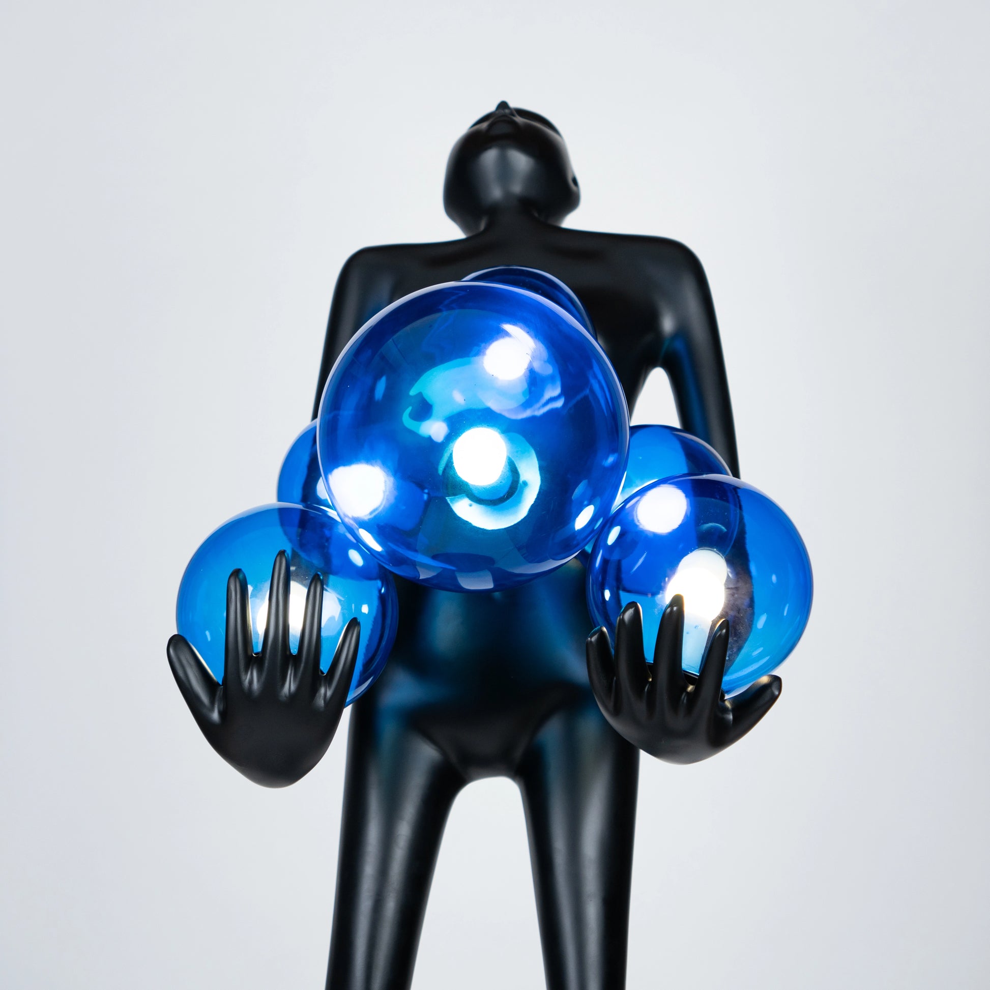Tall matte black sculpture of human figure holding glowing blue light spheres — Azure Radiance Sculpture by Ghar Art, handcrafted illuminated modern home decor accent.