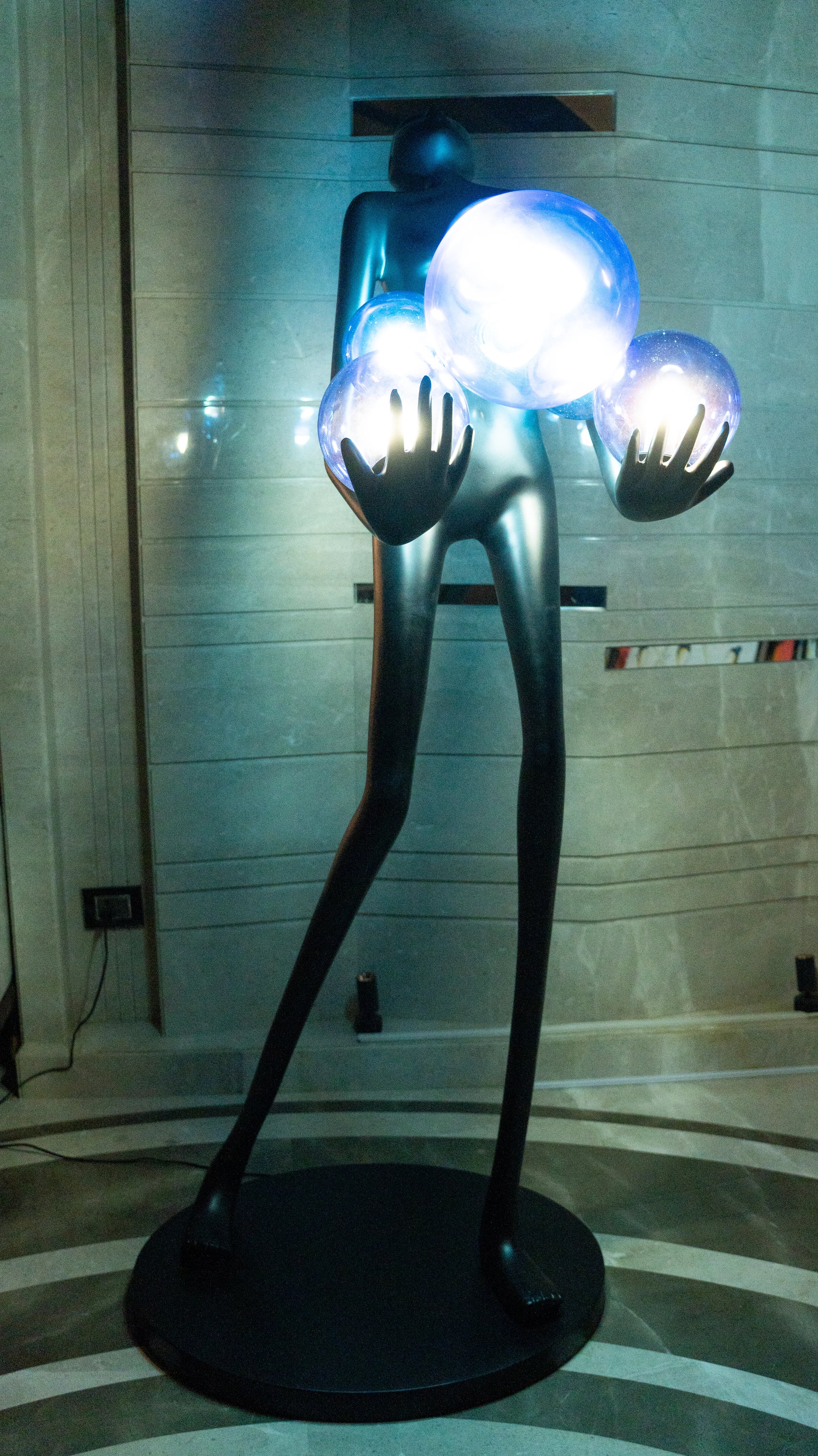 Tall matte black sculpture of human figure holding glowing blue light spheres — Azure Radiance Sculpture by Ghar Art, handcrafted illuminated modern home decor accent.