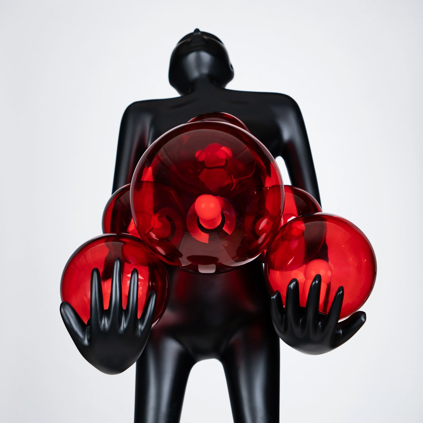 Tall matte black human figure sculpture holding glowing amber light spheres — Ember Radiance Sculpture by Ghar Art, illuminated modern luxury home decor accent.