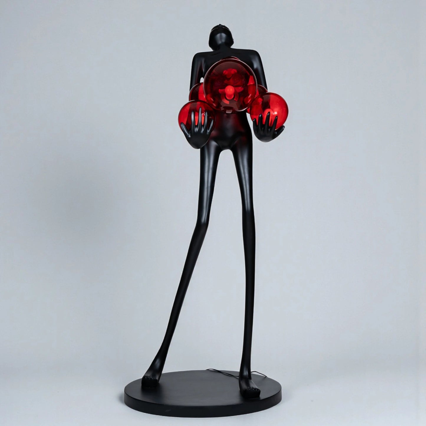 Tall matte black human figure sculpture holding glowing amber light spheres — Ember Radiance Sculpture by Ghar Art, illuminated modern luxury home decor accent.