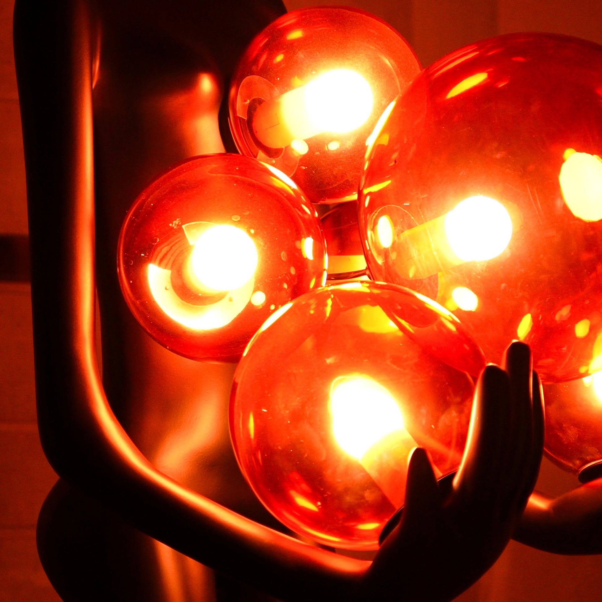 Tall matte black human figure sculpture holding glowing amber light spheres — Ember Radiance Sculpture by Ghar Art, illuminated modern luxury home decor accent.