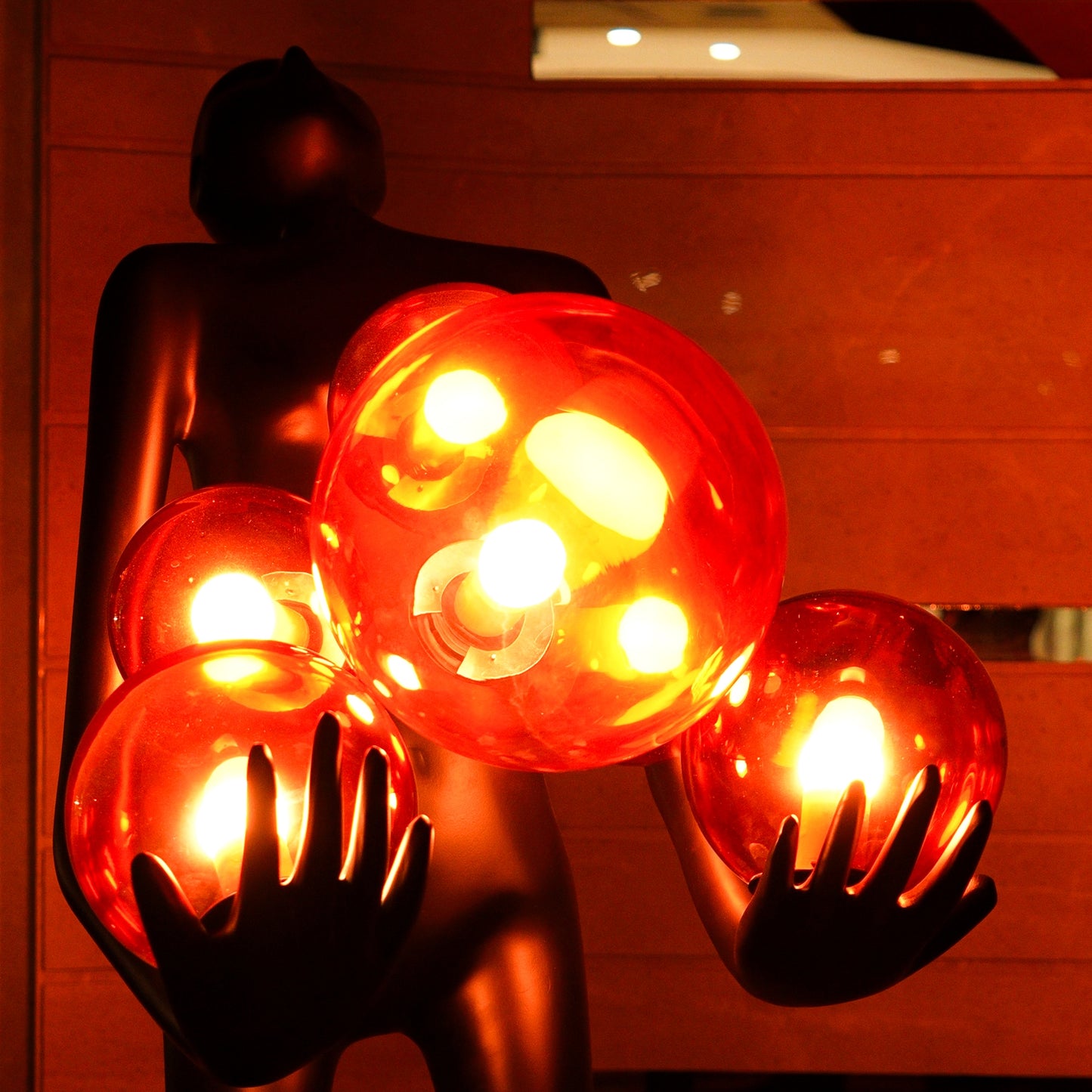 Tall matte black human figure sculpture holding glowing amber light spheres — Ember Radiance Sculpture by Ghar Art, illuminated modern luxury home decor accent.