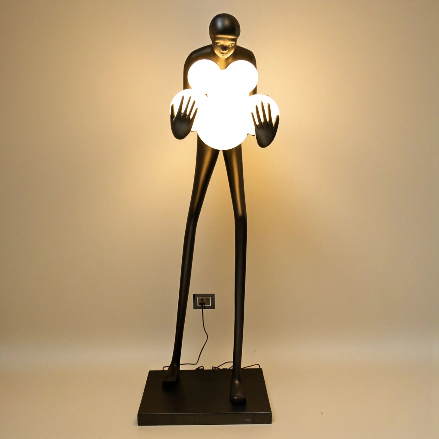 Tall matte black human sculpture holding glowing white orbs