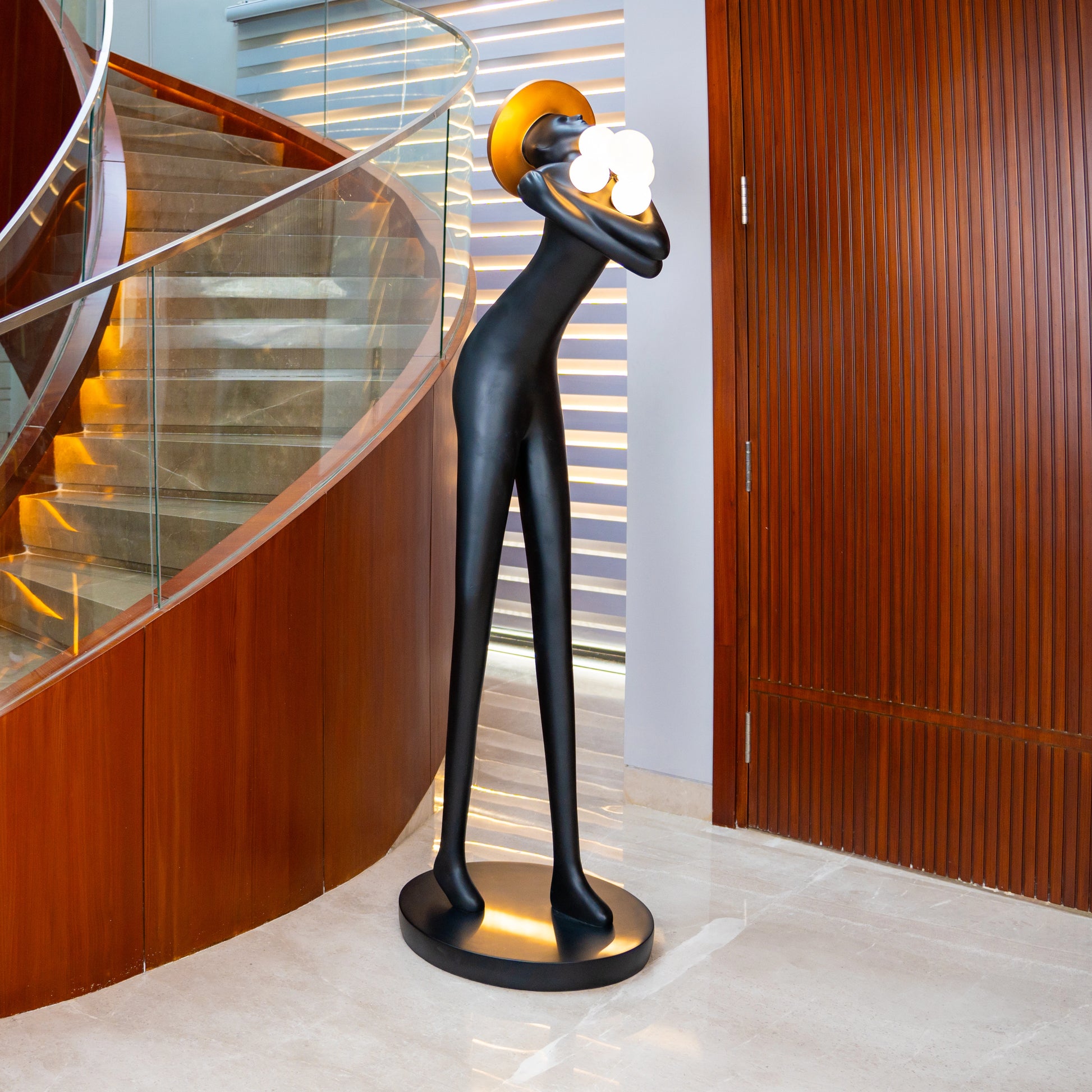 Tall black human-form floor sculpture holding glowing light orbs