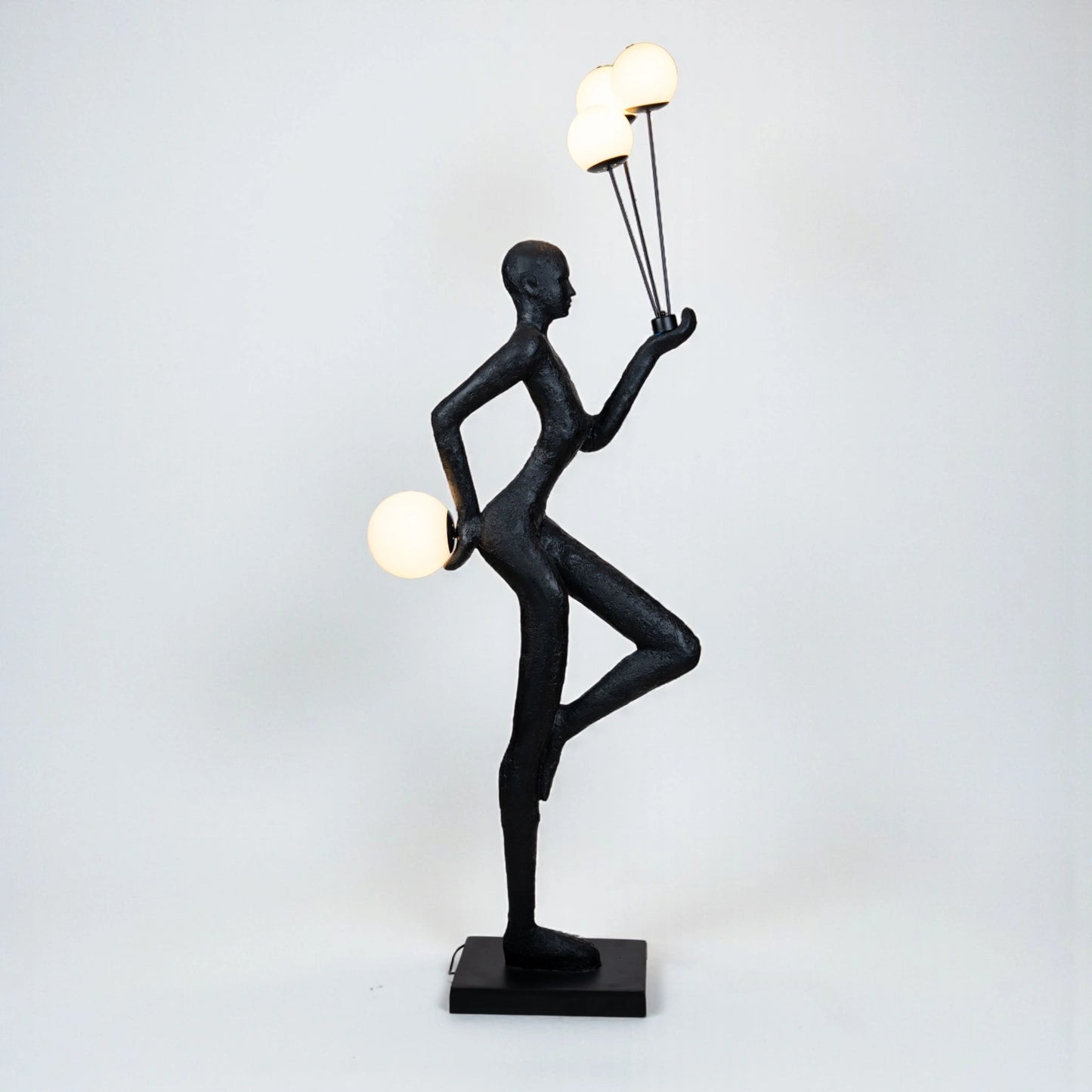 Matte black human-form sculpture holding illuminated orbs