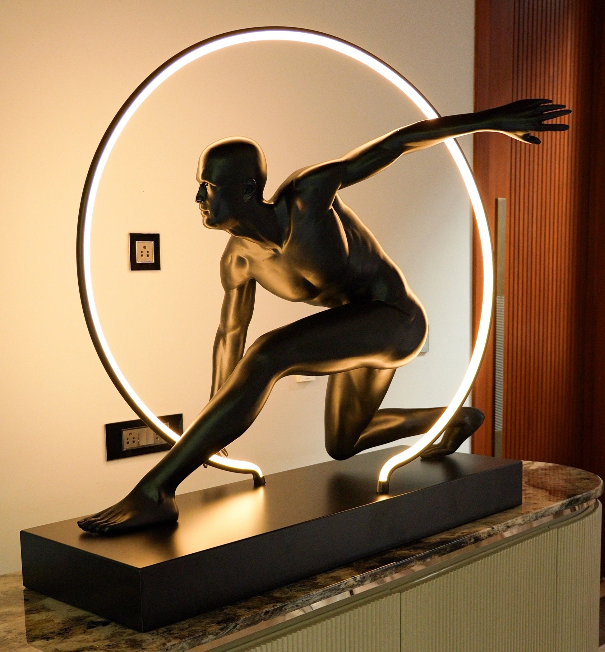 Matte black illuminated human motion sculpture with halo light ring on rectangular base