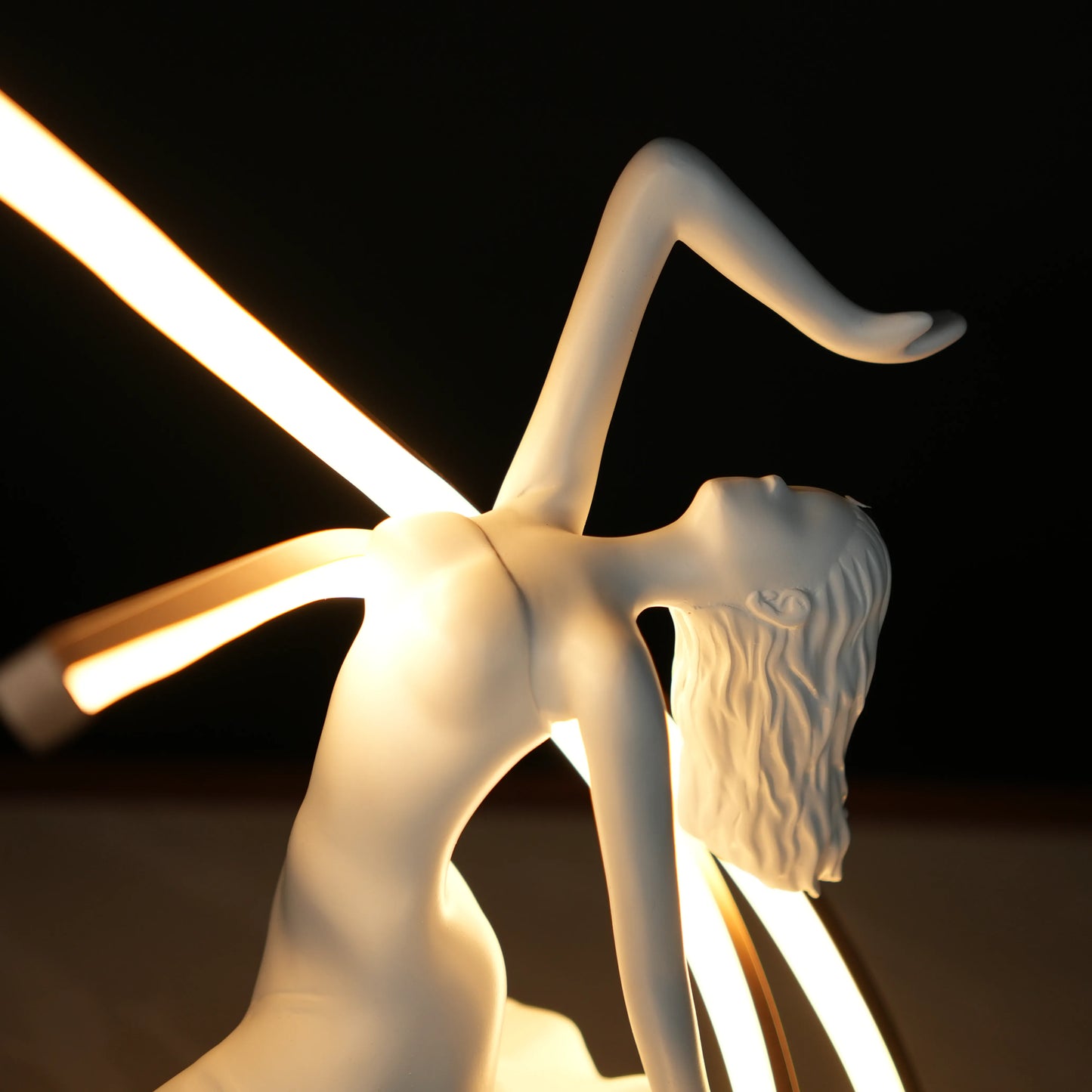 Small white sculpture lamp of a dancing woman with sweeping LED arcs and a glowing orb on a black base.