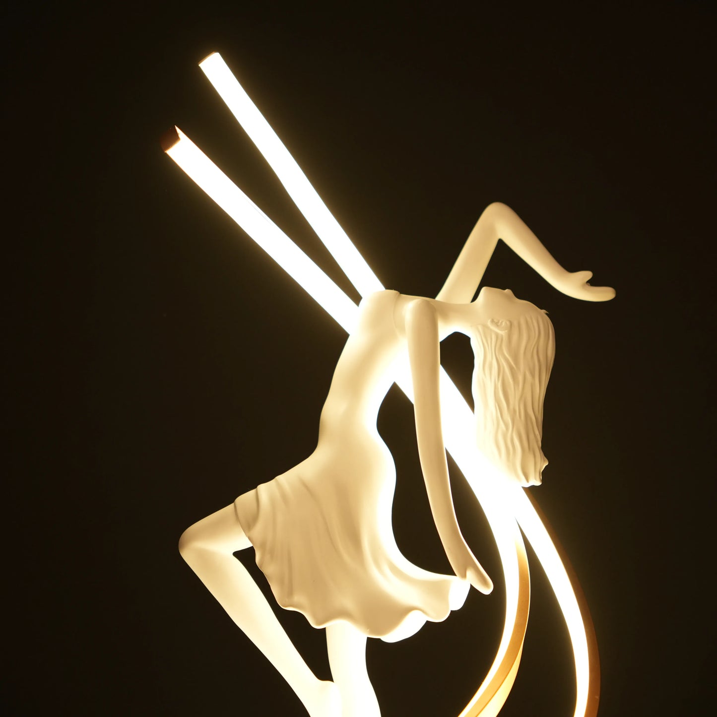 Small white sculpture lamp of a dancing woman with sweeping LED arcs and a glowing orb on a black base.