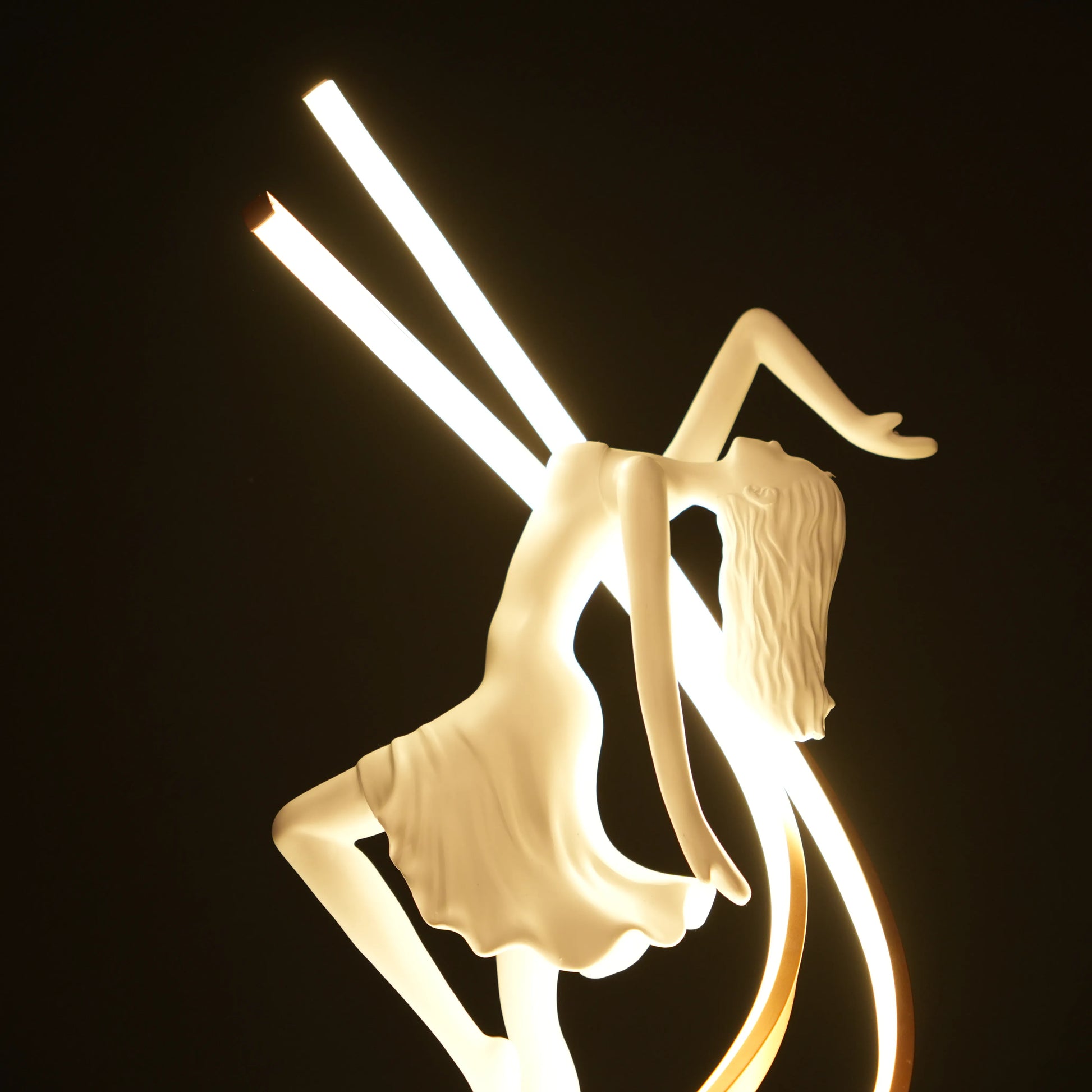 Small white sculpture lamp of a dancing woman with sweeping LED arcs and a glowing orb on a black base.