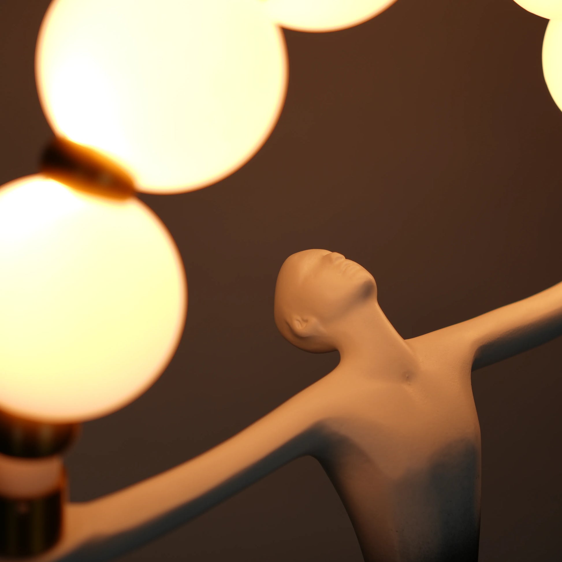 Small black-white ombre sculptural lamp featuring an elongated human figure lifting an arc of warm glowing spheres with gold accents on a round base.