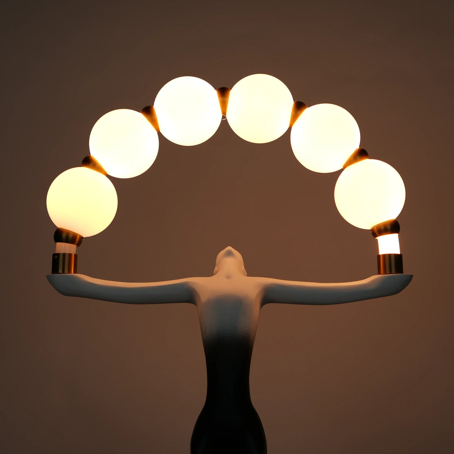 Small black-white ombre sculptural lamp featuring an elongated human figure lifting an arc of warm glowing spheres with gold accents on a round base.