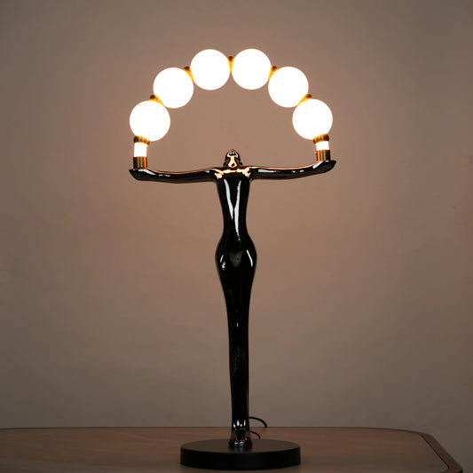 Small electroplated black human-form sculpture holding an arc of glowing warm orb lights with gold accents on a black circular base.
