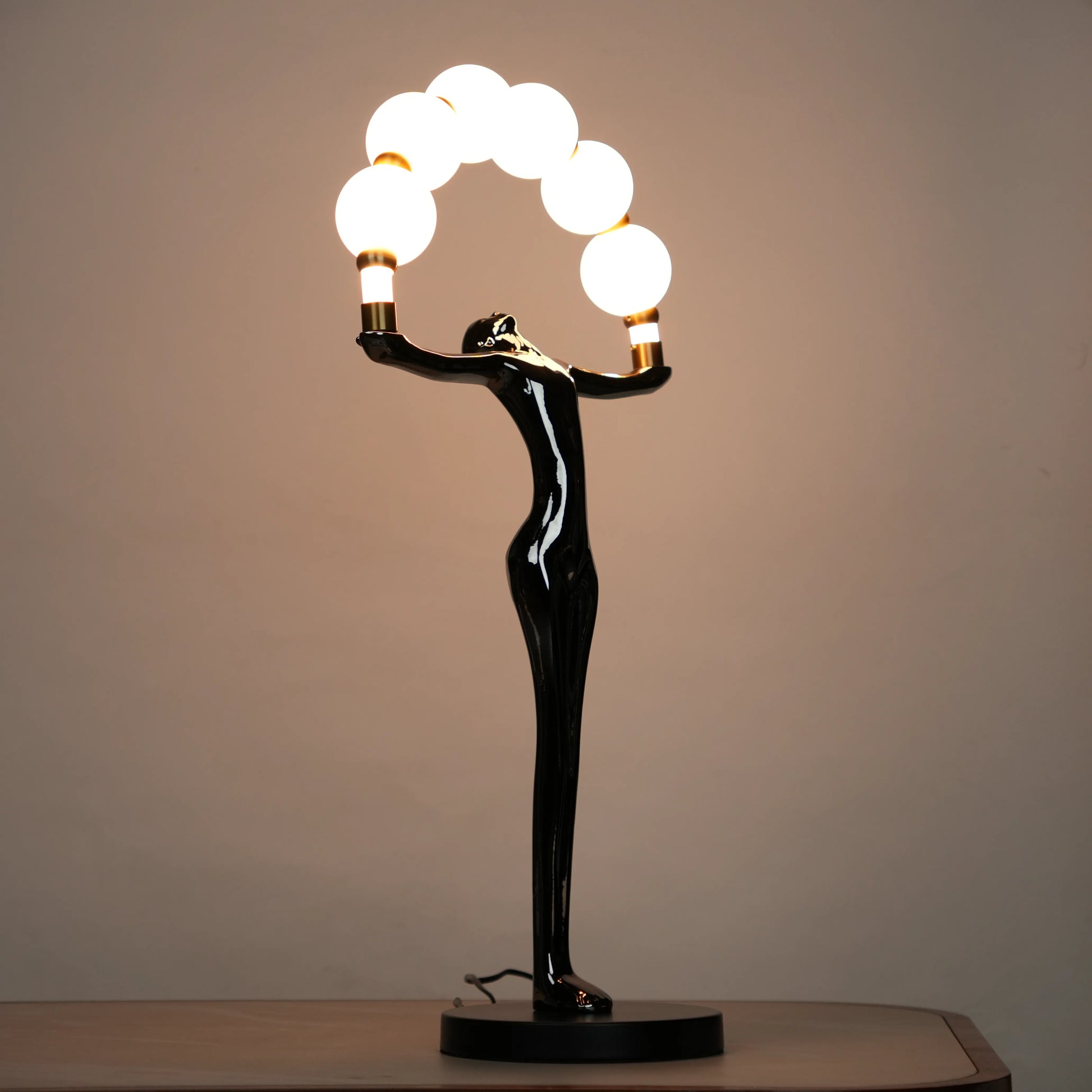 Small electroplated black human-form sculpture holding an arc of glowing warm orb lights with gold accents on a black circular base.
