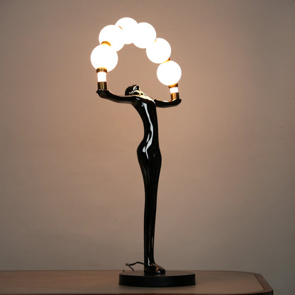 Small electroplated black human-form sculpture holding an arc of glowing warm orb lights with gold accents on a black circular base.