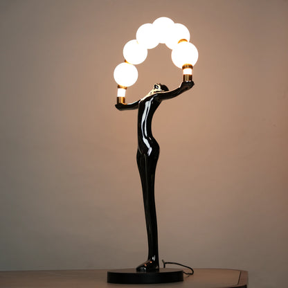 Small electroplated black human-form sculpture holding an arc of glowing warm orb lights with gold accents on a black circular base.