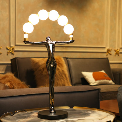 Small electroplated black human-form sculpture holding an arc of glowing warm orb lights with gold accents on a black circular base.