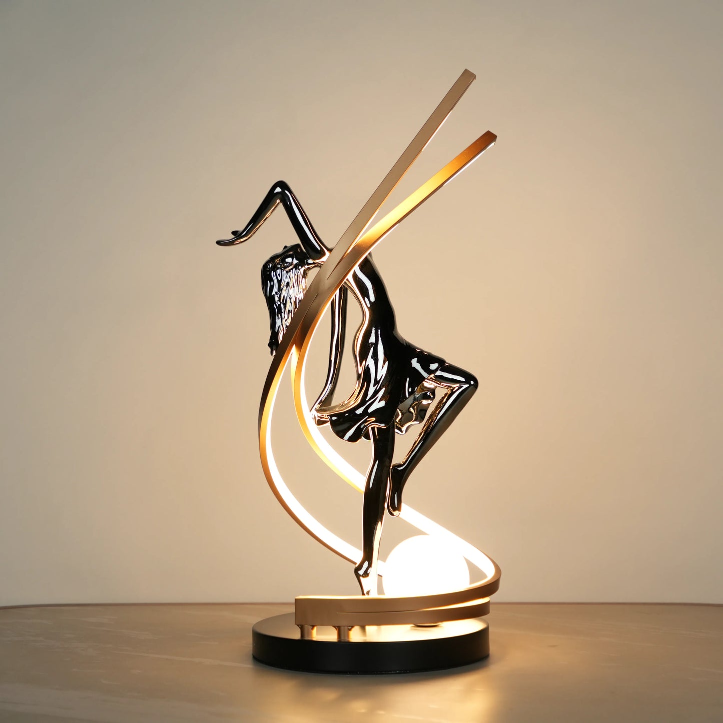 Small electroplated black sculpture lamp of a dancing woman with curved LED arcs and warm glowing orb.
