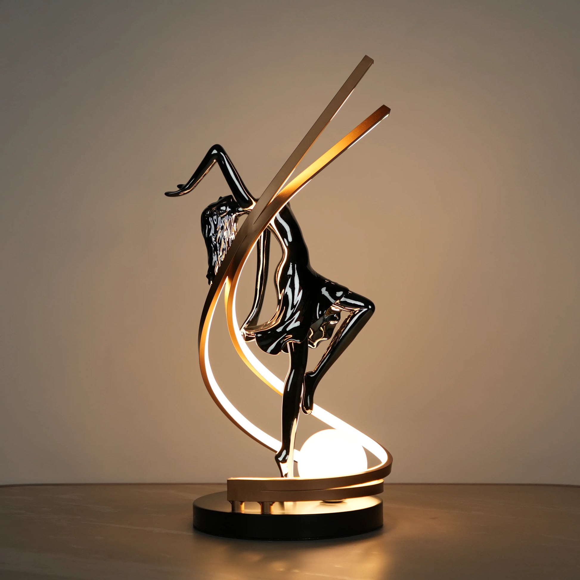Small electroplated black sculpture lamp of a dancing woman with curved LED arcs and warm glowing orb.