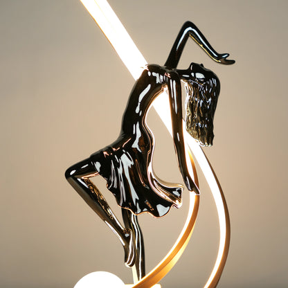 Small electroplated black sculpture lamp of a dancing woman with curved LED arcs and warm glowing orb.