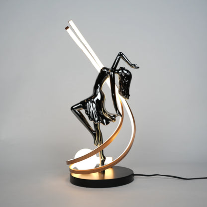 Small electroplated black sculpture lamp of a dancing woman with curved LED arcs and warm glowing orb.