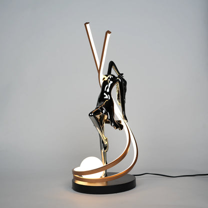 Small electroplated black sculpture lamp of a dancing woman with curved LED arcs and warm glowing orb.