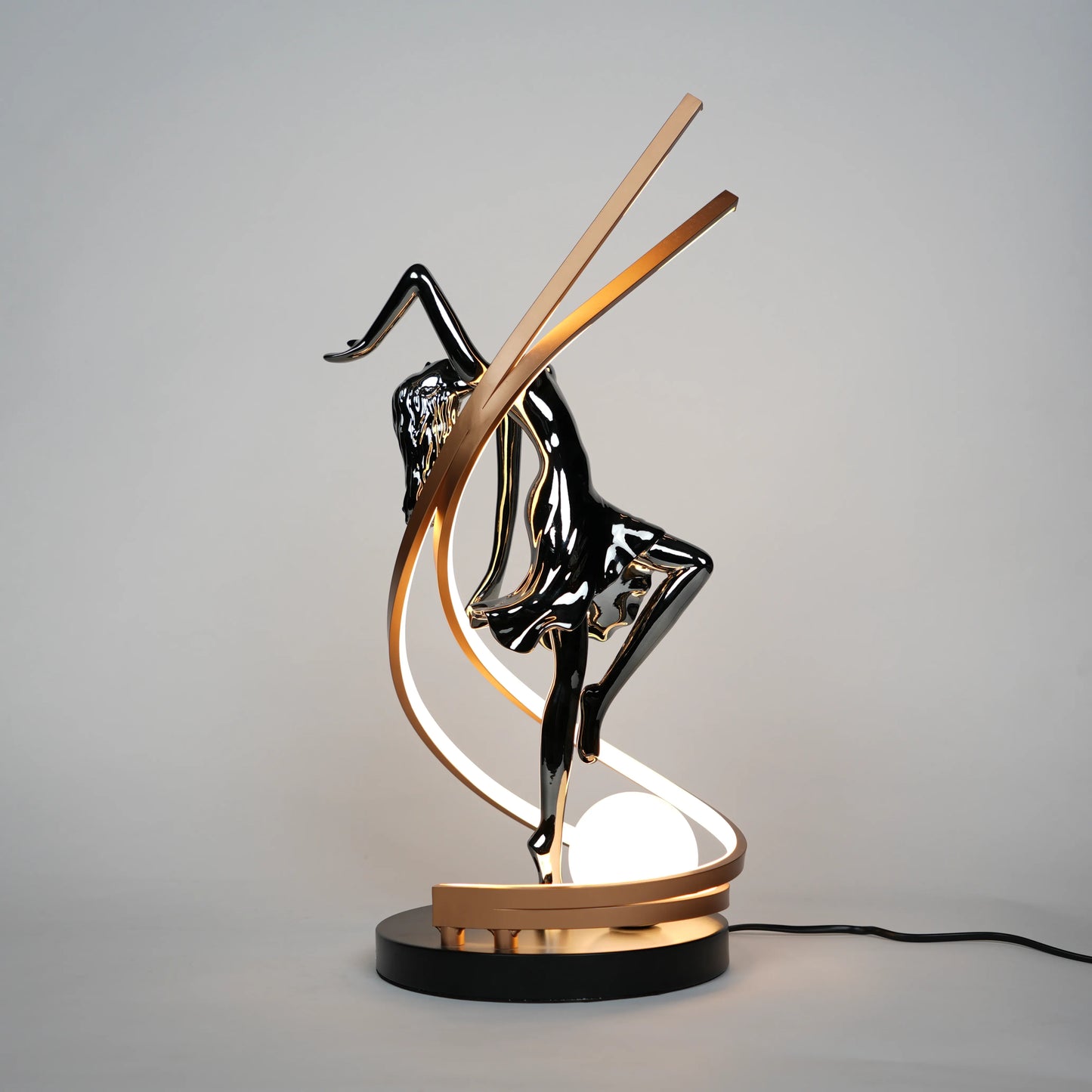 Small electroplated black sculpture lamp of a dancing woman with curved LED arcs and warm glowing orb.