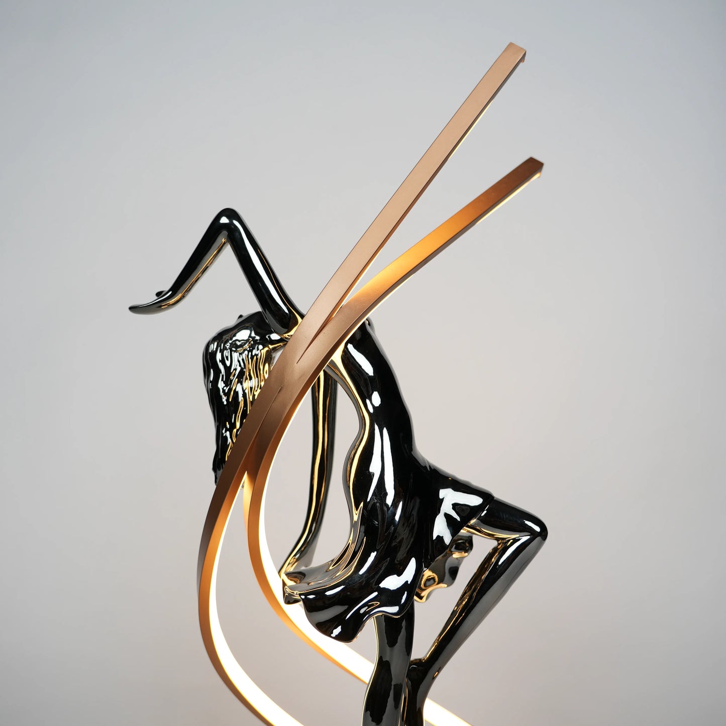 Small electroplated black sculpture lamp of a dancing woman with curved LED arcs and warm glowing orb.