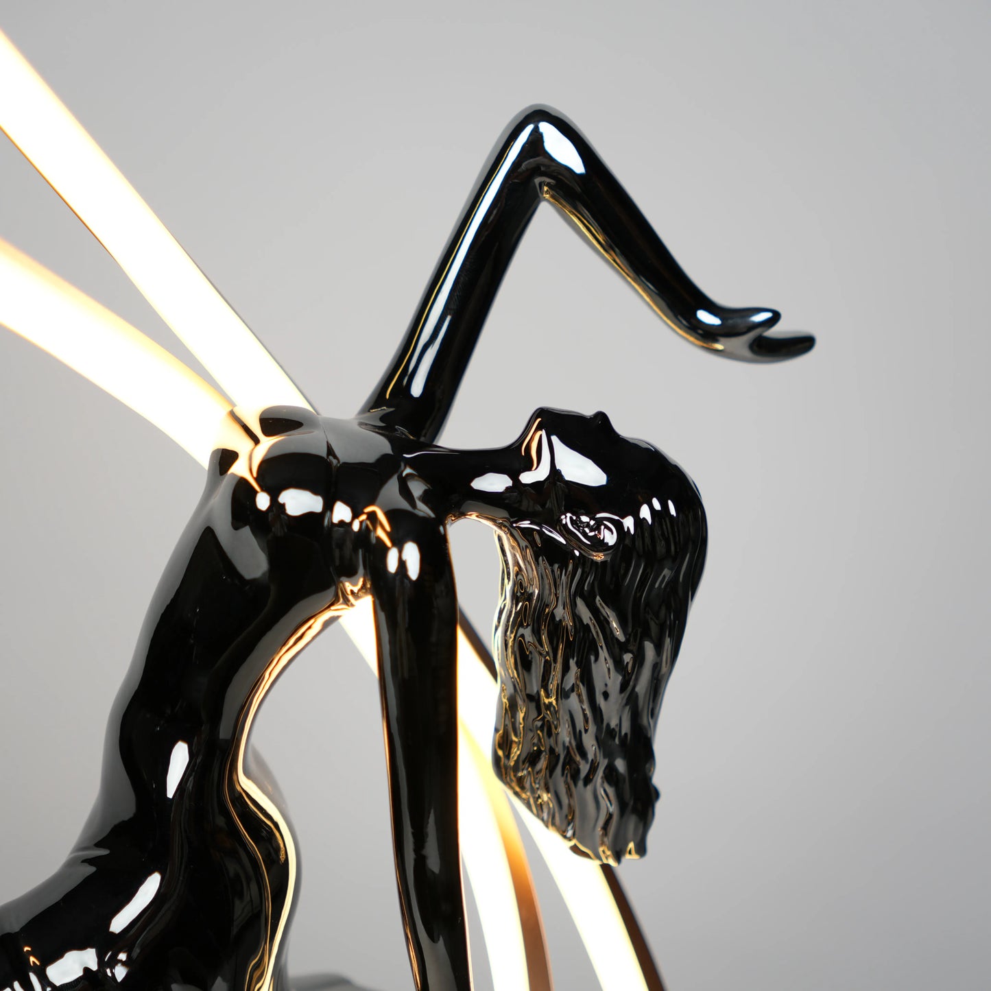 Small electroplated black sculpture lamp of a dancing woman with curved LED arcs and warm glowing orb.