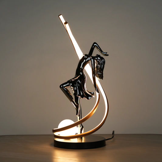 Small electroplated black sculpture lamp of a dancing woman with curved LED arcs and warm glowing orb.