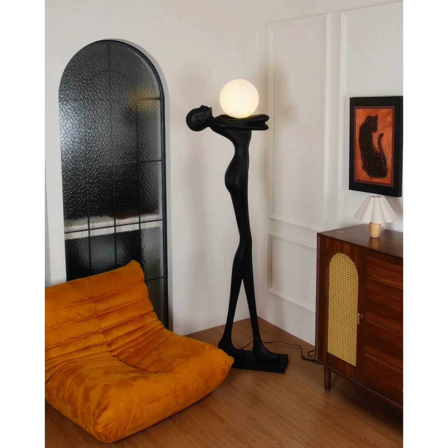 Tall matte black human sculpture floor lamp holding a glowing orb in a modern interior setting.”