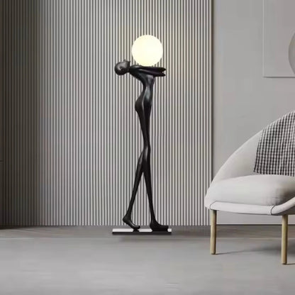 Tall matte black human sculpture floor lamp holding a glowing orb in a modern interior setting.”