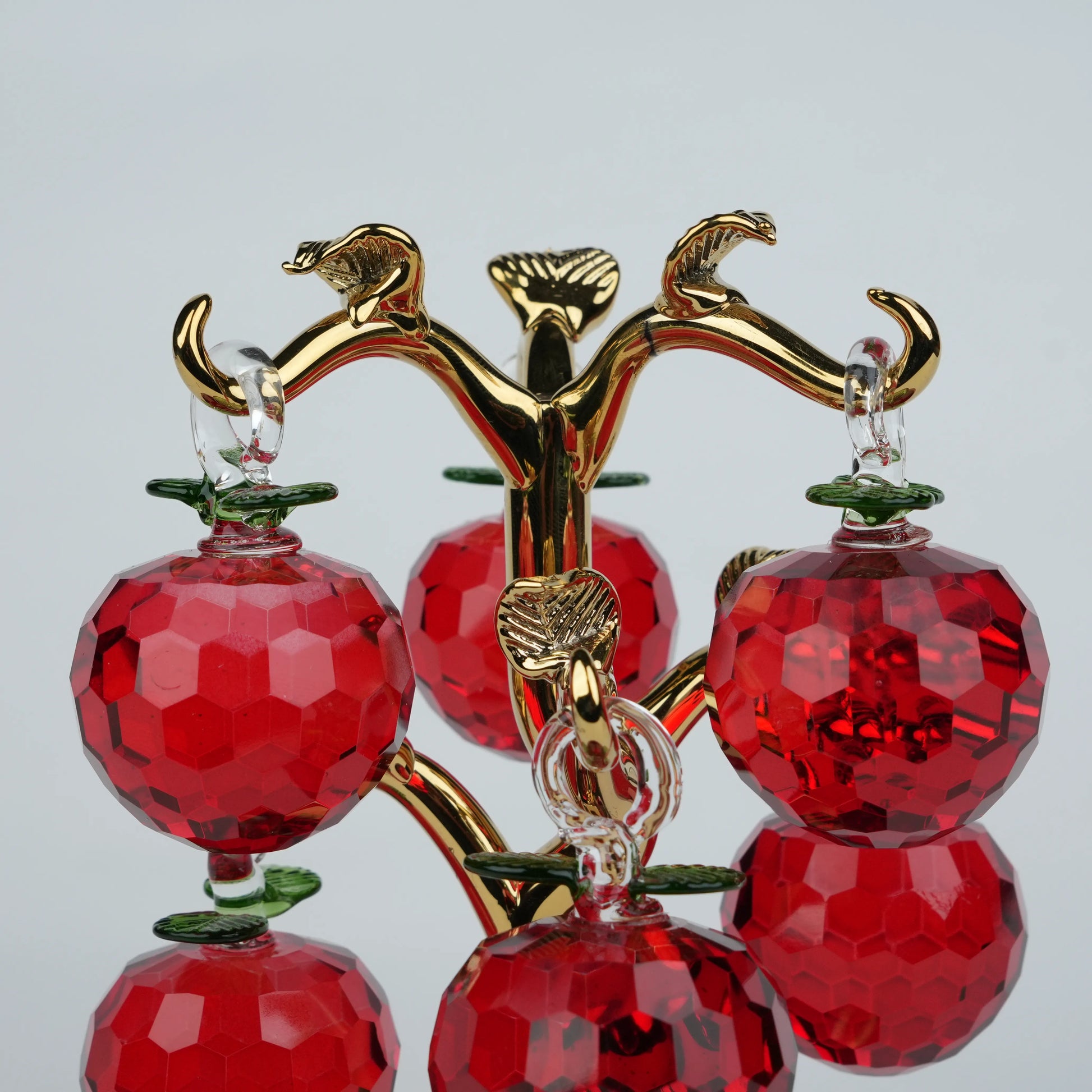 Dense cluster golden crystal apple tree with multiple red faceted apples on a mirrored base.