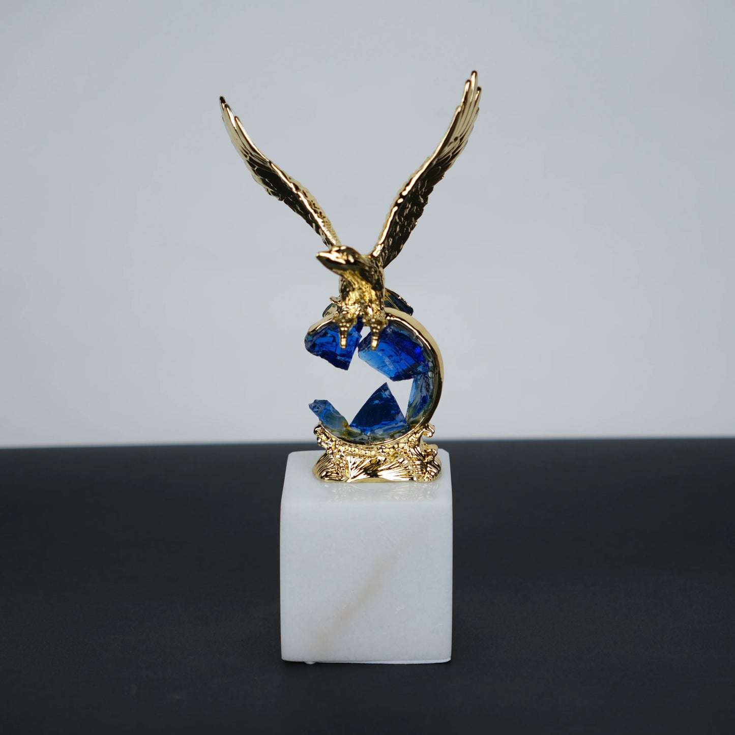 Golden eagle rising from blue crystal wave sculpture on white marble base