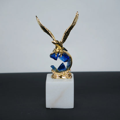 Golden eagle rising from blue crystal wave sculpture on white marble base