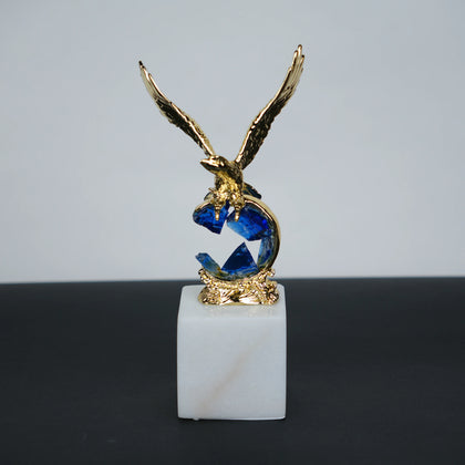 Golden eagle rising from blue crystal wave sculpture on white marble base