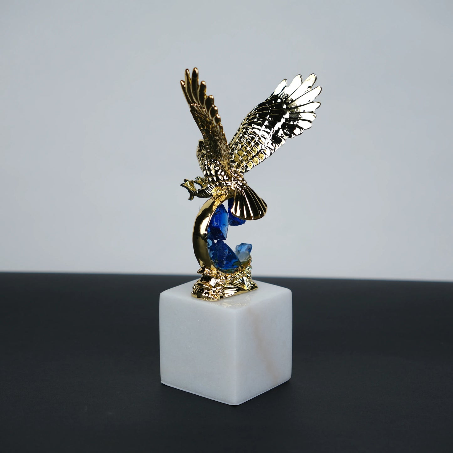 Golden eagle rising from blue crystal wave sculpture on white marble base