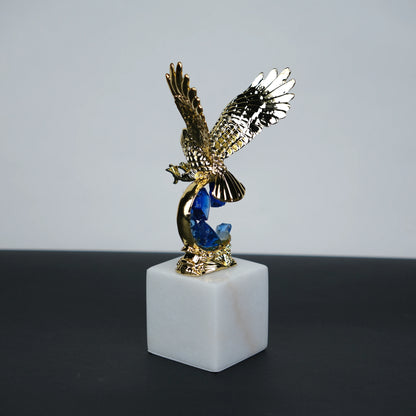 Golden eagle rising from blue crystal wave sculpture on white marble base
