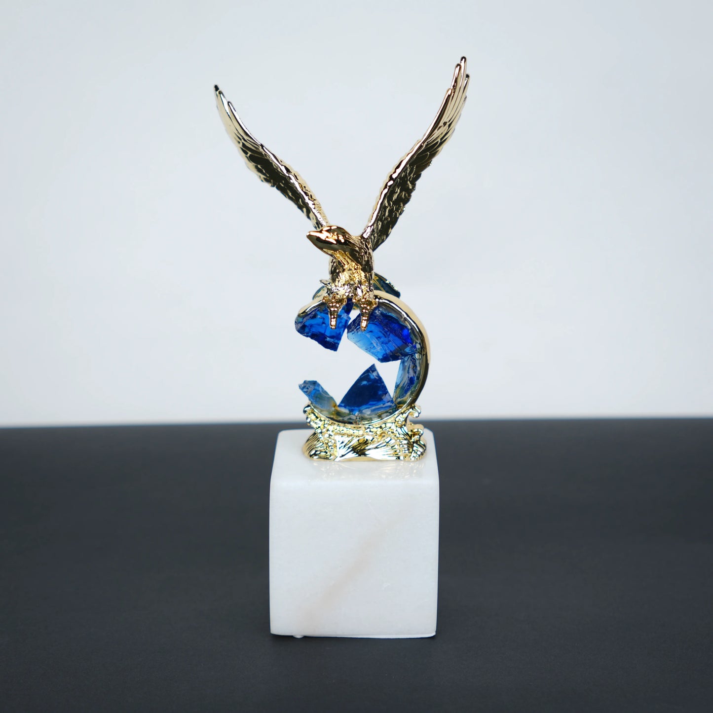 Golden eagle rising from blue crystal wave sculpture on white marble base