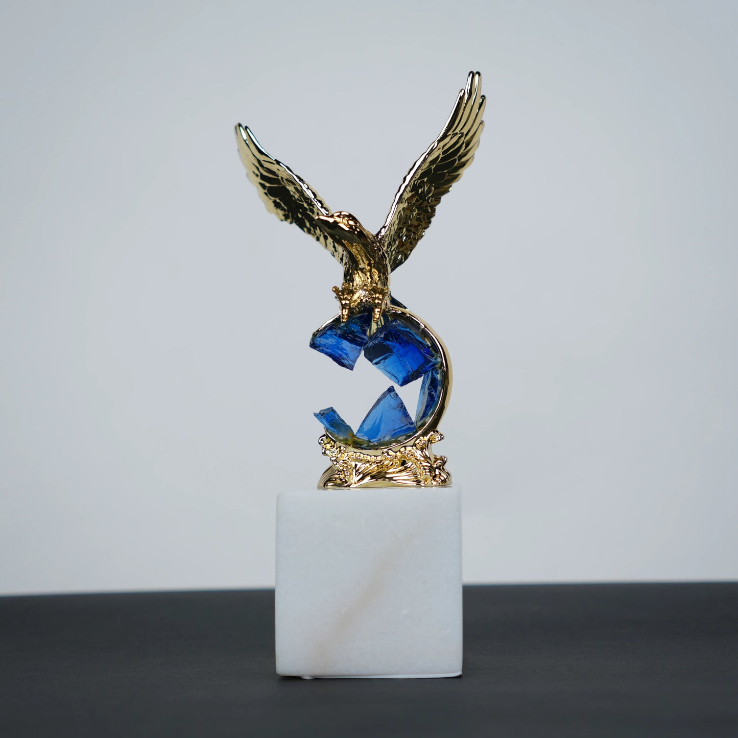 Golden eagle rising from blue crystal wave sculpture on white marble base