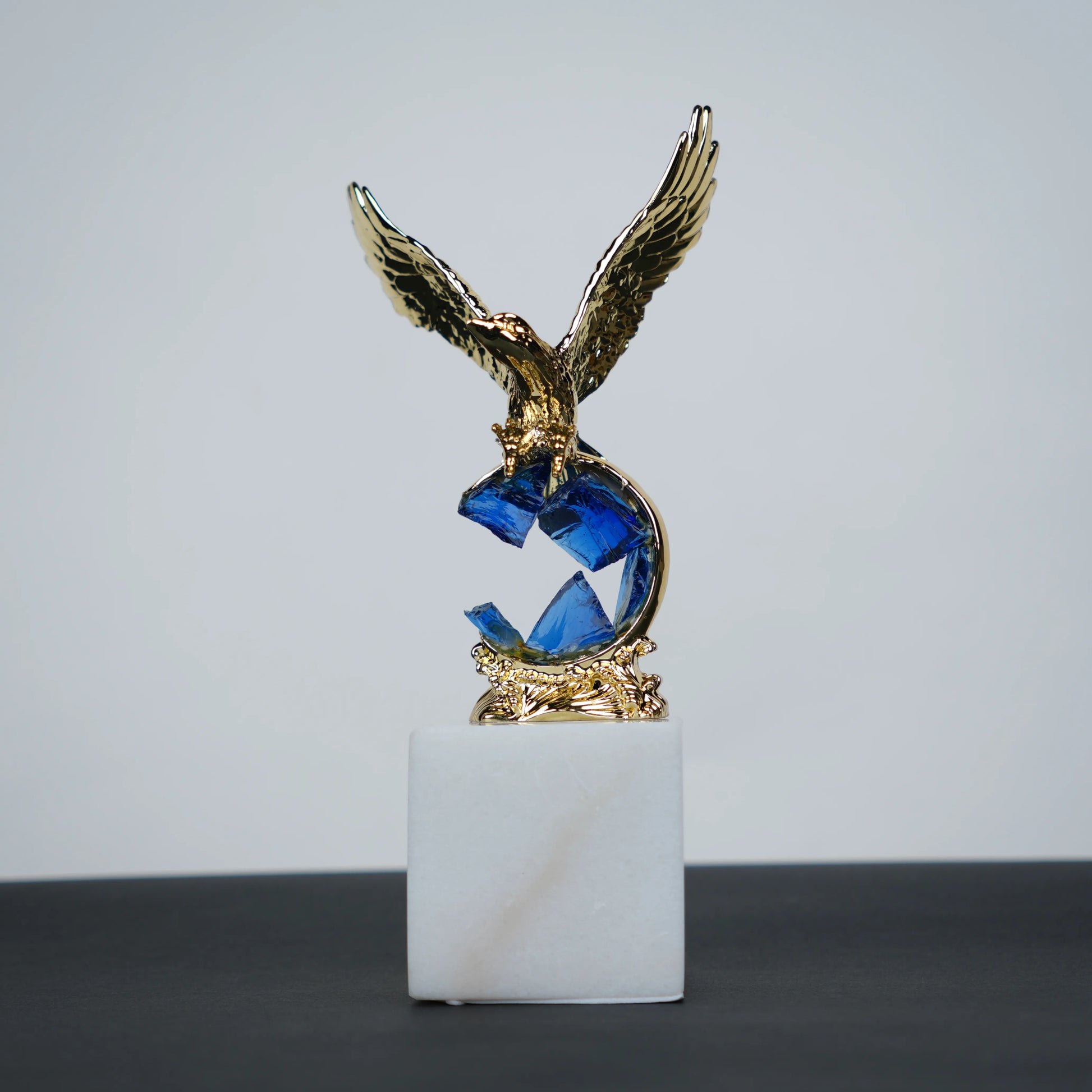 Golden eagle rising from blue crystal wave sculpture on white marble base