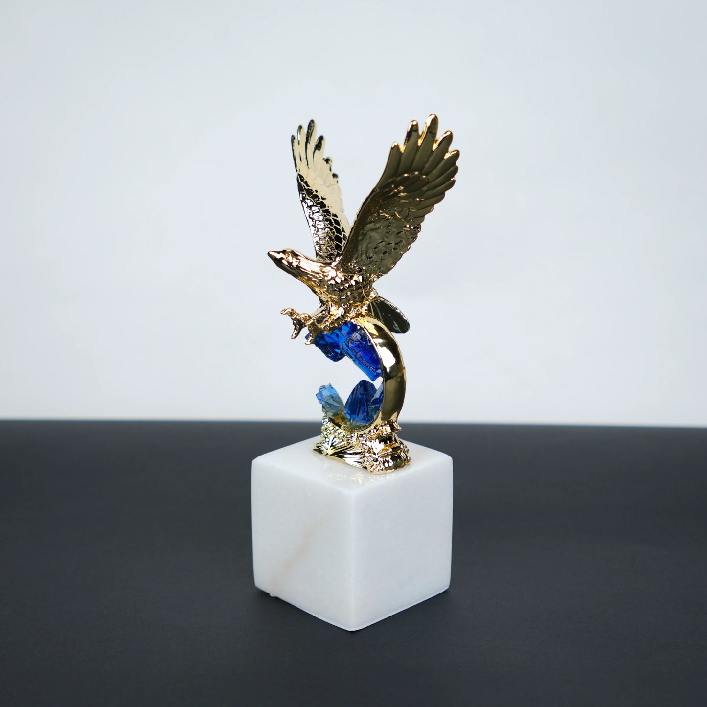 Golden eagle rising from blue crystal wave sculpture on white marble base