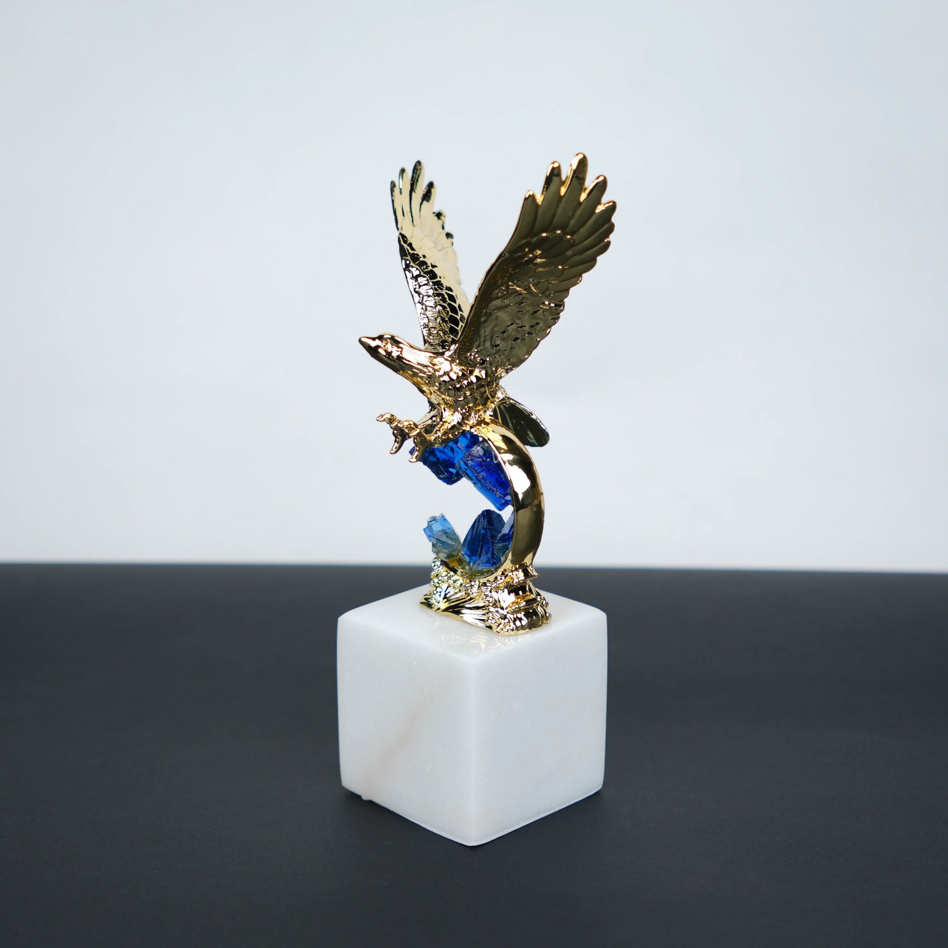 Golden eagle rising from blue crystal wave sculpture on white marble base