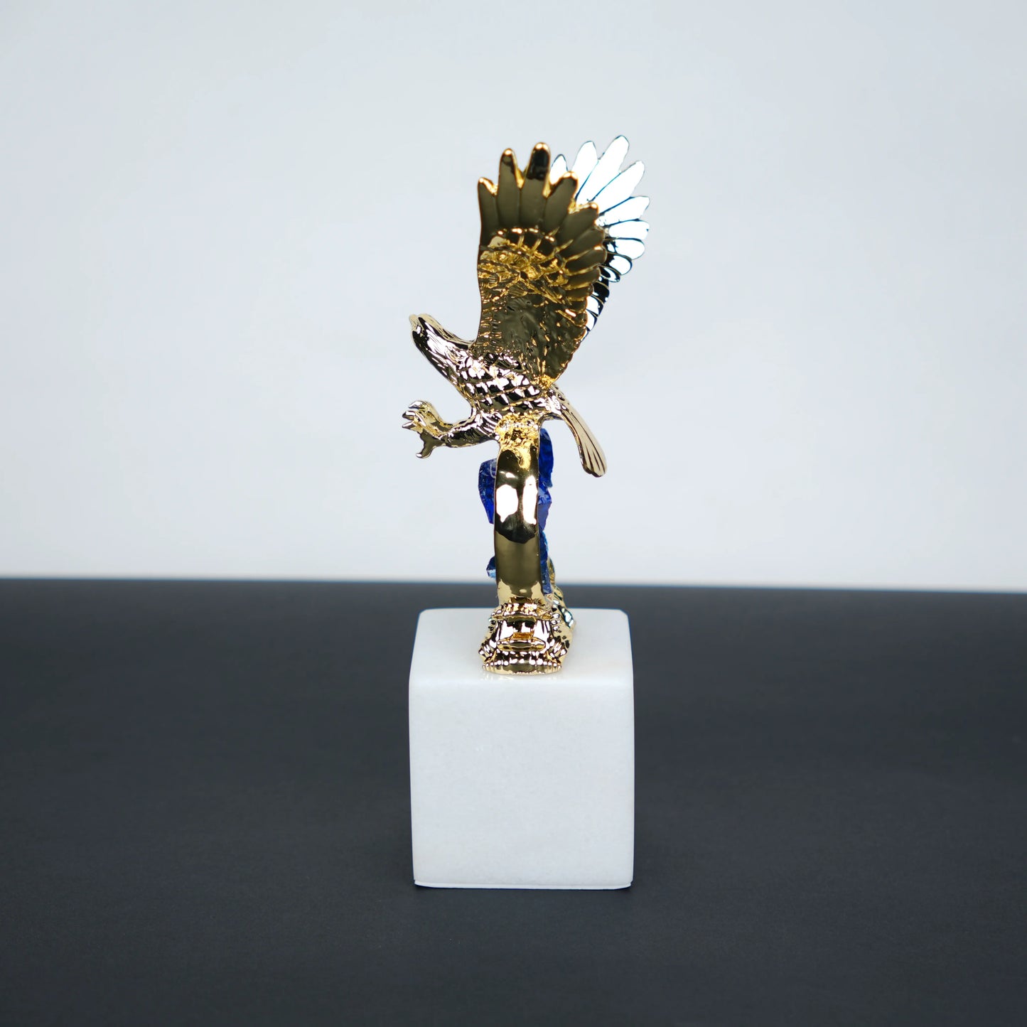 Golden eagle rising from blue crystal wave sculpture on white marble base